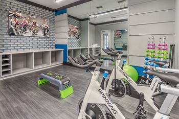 A Spinning bike is in the foreground of a brightly lit gym at Crabtree Lakeside Apartments, North Carolina, 27612